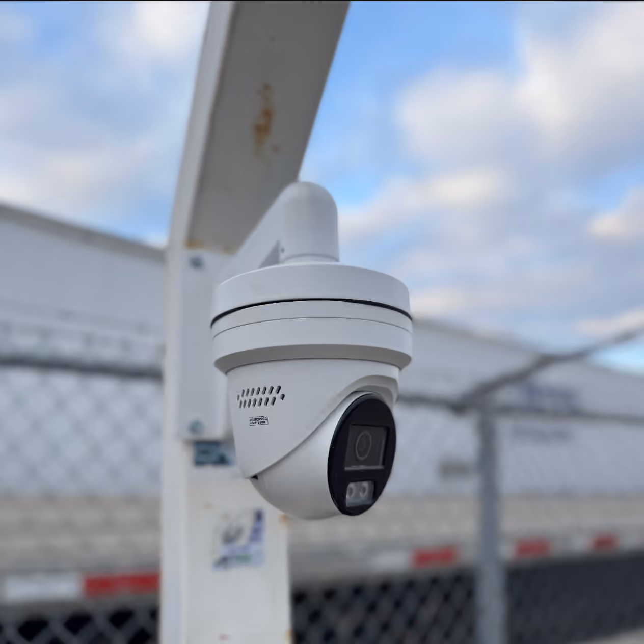 White dome security camera installed outdoors near a fenced area