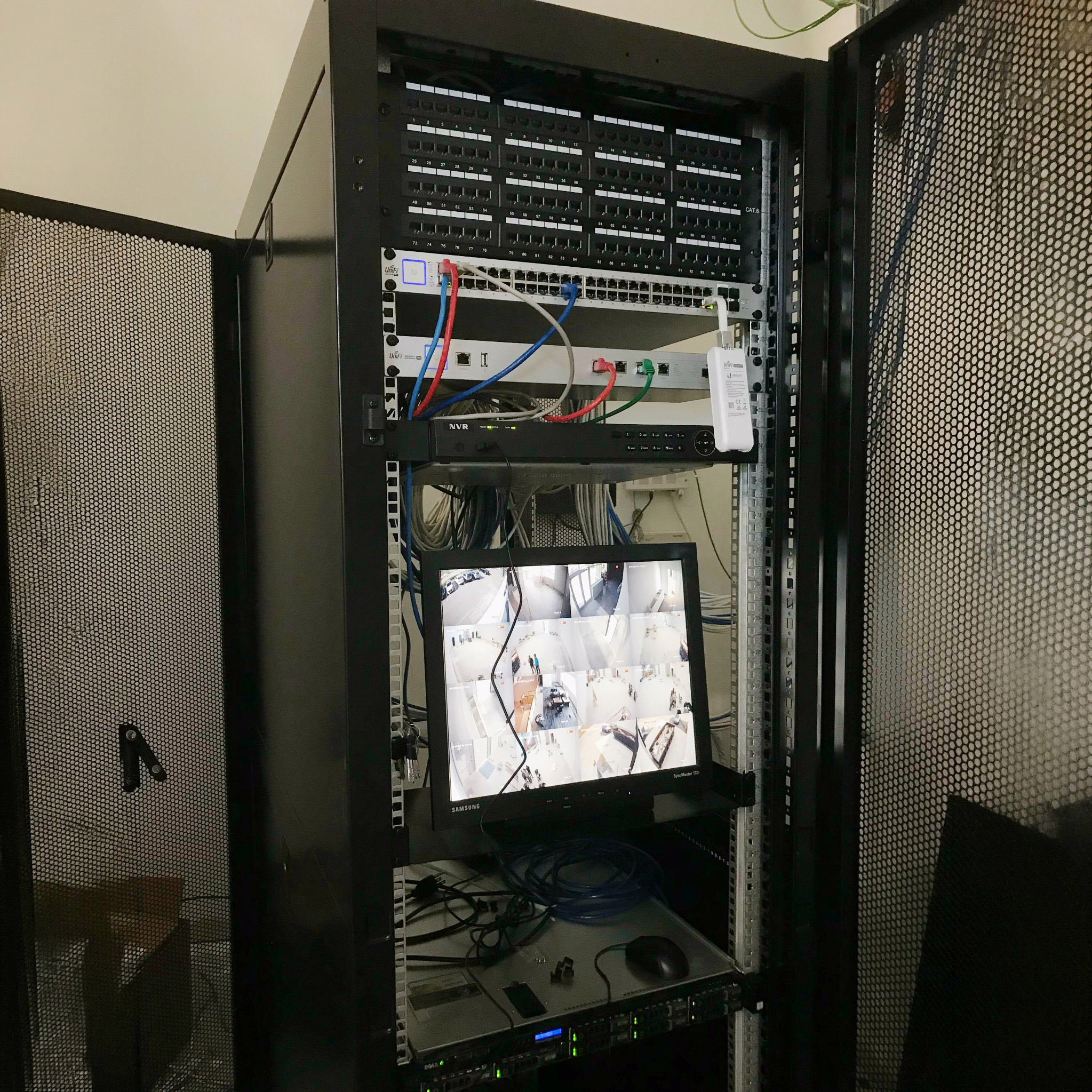 Commercial equipment rack with patch panels, network switches, and a security camera monitor