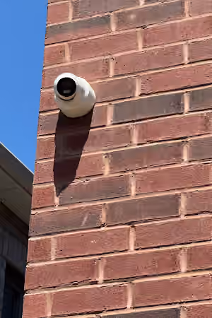 White security camera mounted high on a red brick exterior wall.