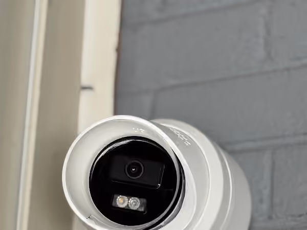 Close-up of a white outdoor security camera against a painted brick wall.