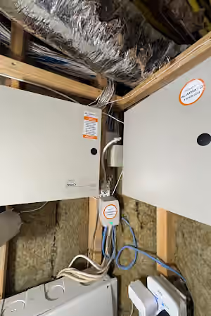 Security system cabinets and connected cables mounted on exposed basement framing.