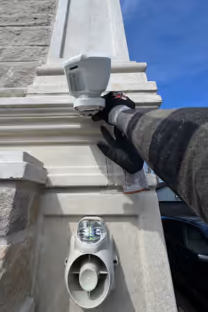 Gloved hands adjusting an outdoor security camera on a stone exterior wall.