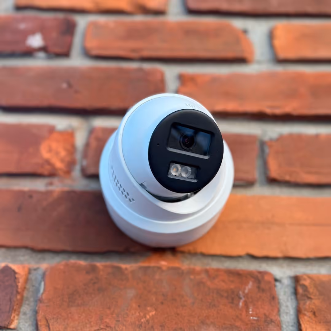 White outdoor security camera mounted on a red brick wall