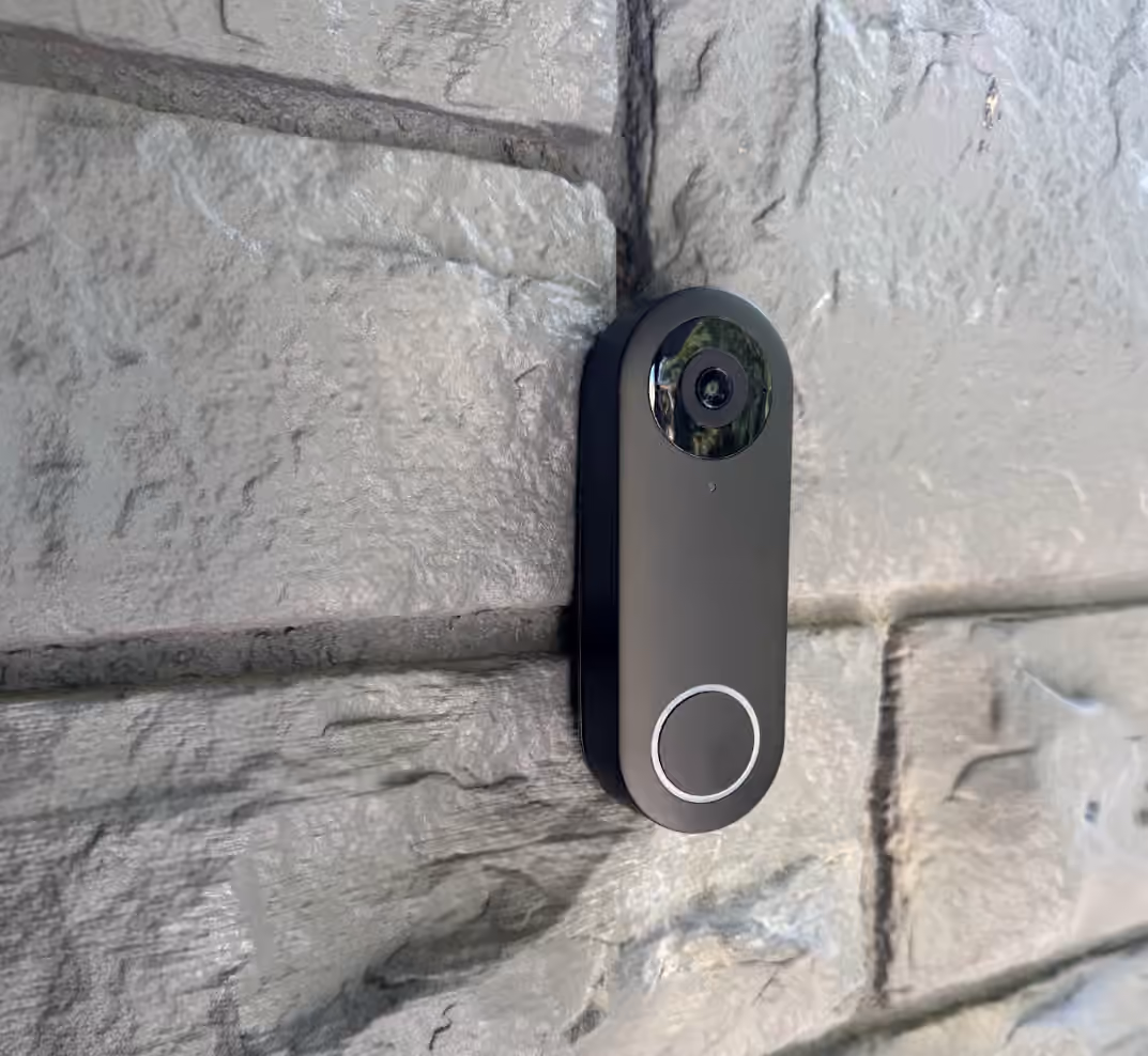 Black video doorbell installed on a light stone wall