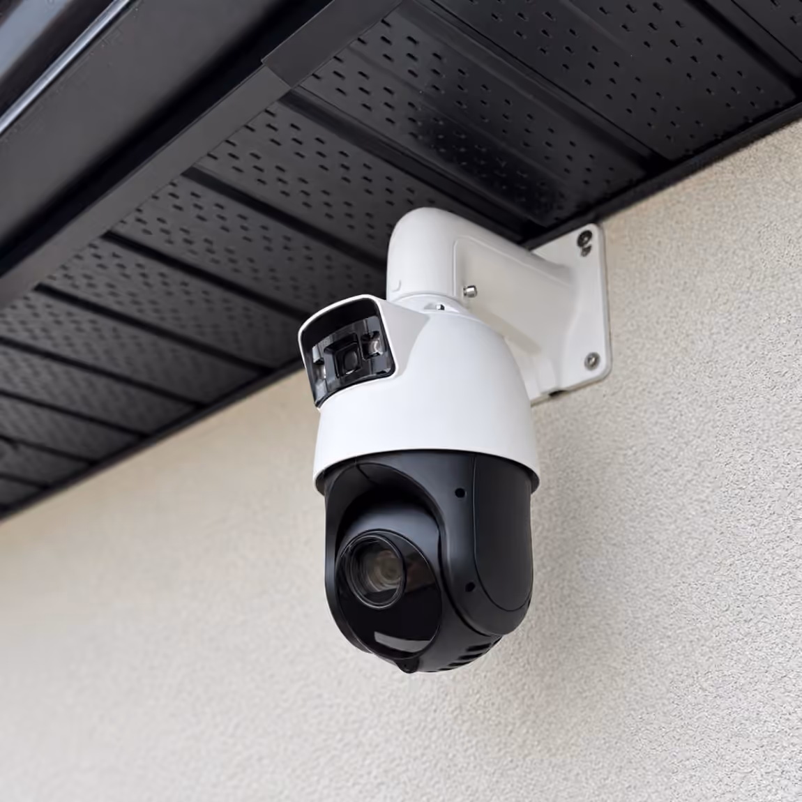 White outdoor PTZ security camera mounted beneath a roof eave