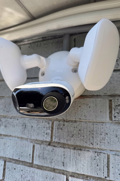 Reolink floodlight security camera mounted beneath a roof overhang.