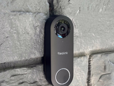 Black Reolink video doorbell on a painted brick wall.