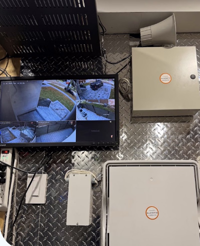 Security monitor, alarm enclosures and network equipment on a metal-panelled wall.