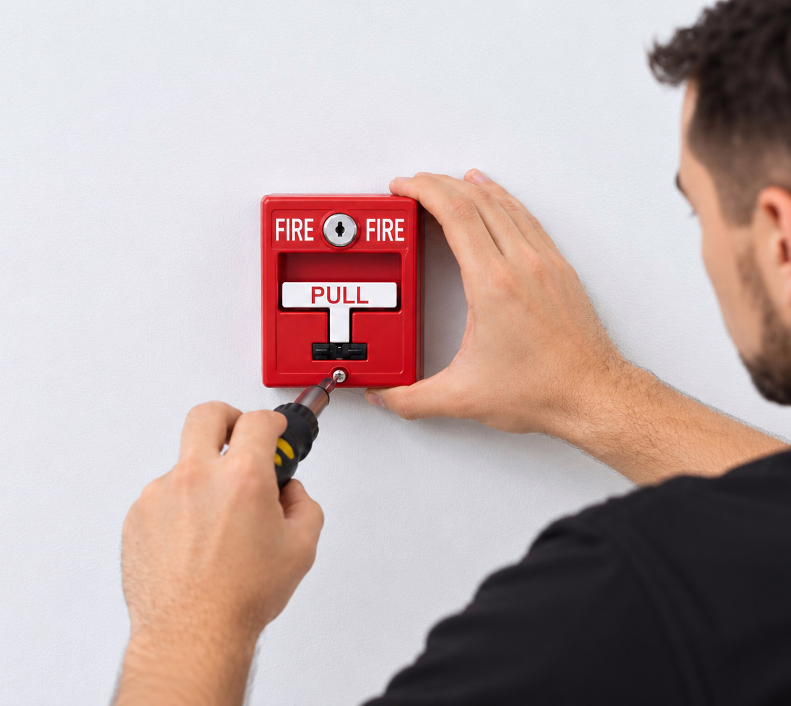 Technician installing a red fire alarm pull station on a wall